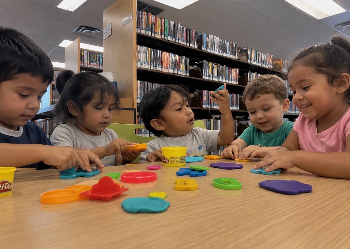 Toddlers shaping play-dough letters together at a low table